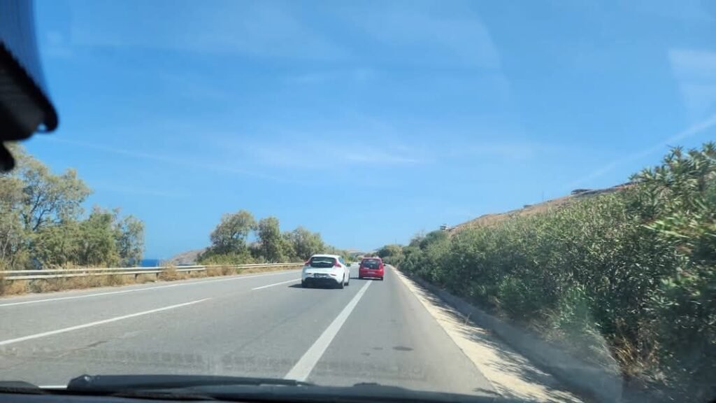 When driving in Crete, be like the red car: pull onto the hard shoulder to let faster traffic pass. It's standard Cretan road etiquette that keeps everyone happy.