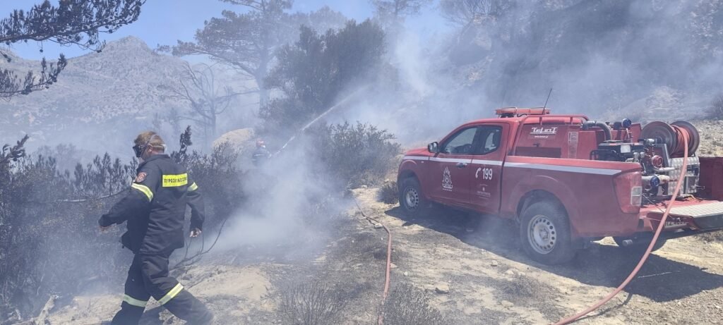 Firefighters suppressing hotspots in southeastern Crete, with fire truck supporting operations. While the main fires are extinguished, crews remain on site to prevent any flare-ups from reigniting. 
