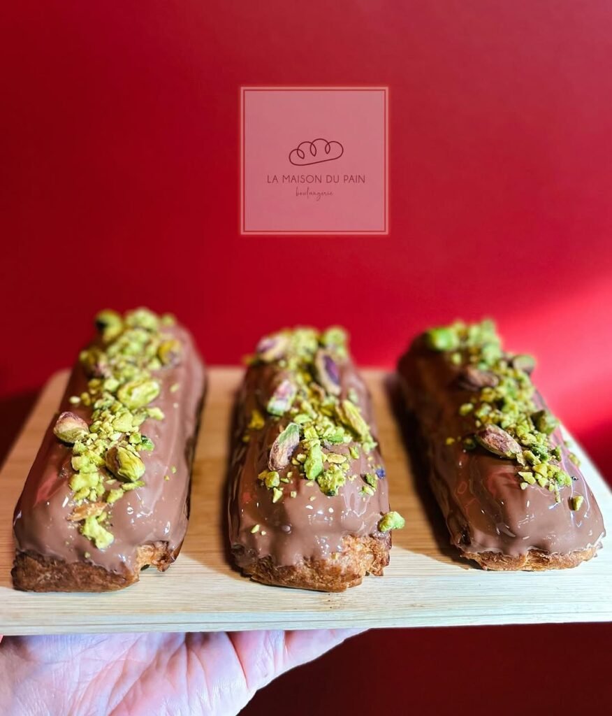 Exquisite chocolate éclairs topped with crushed pistachios from La Maison du Pain, where authentic French pâtisserie techniques and beautiful presentation showcase the "L'art de vivre" philosophy that brings genuine Parisian boulangerie traditions to Heraklion.