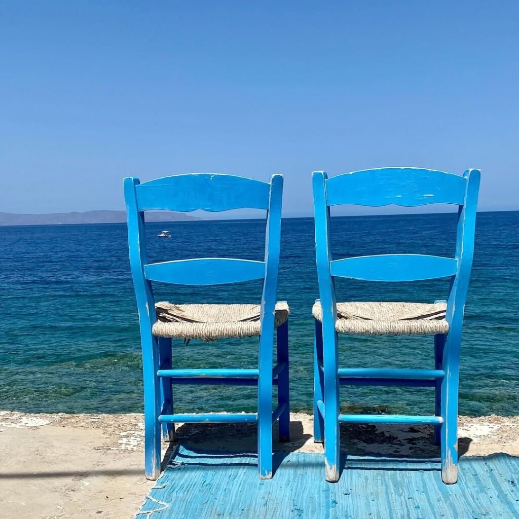 Two iconic blue chairs overlook the crystal-clear waters of Crete, where the healing tradition of seaside contemplation continues today. 