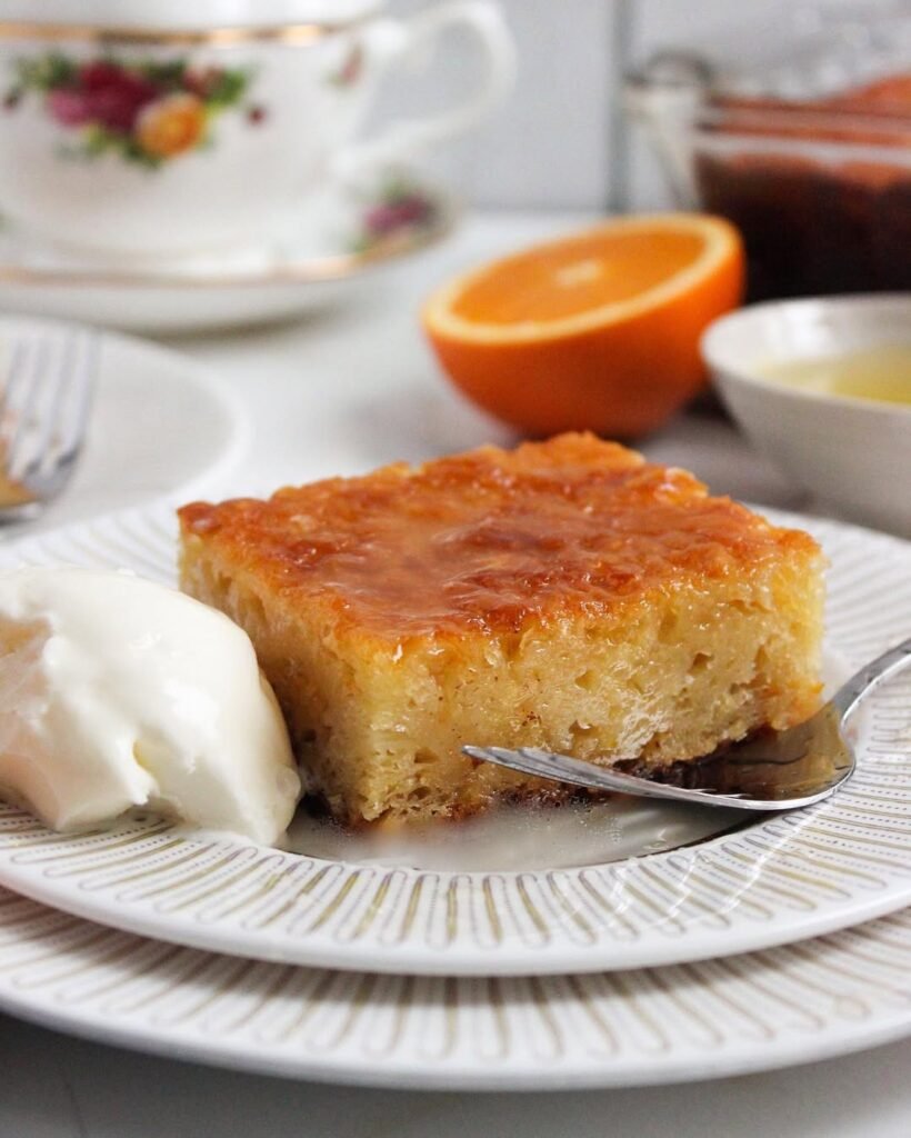 Moist and citrusy portokalopita served chilled with cream, showcasing the bright orange flavors that make this dessert so refreshing. 
