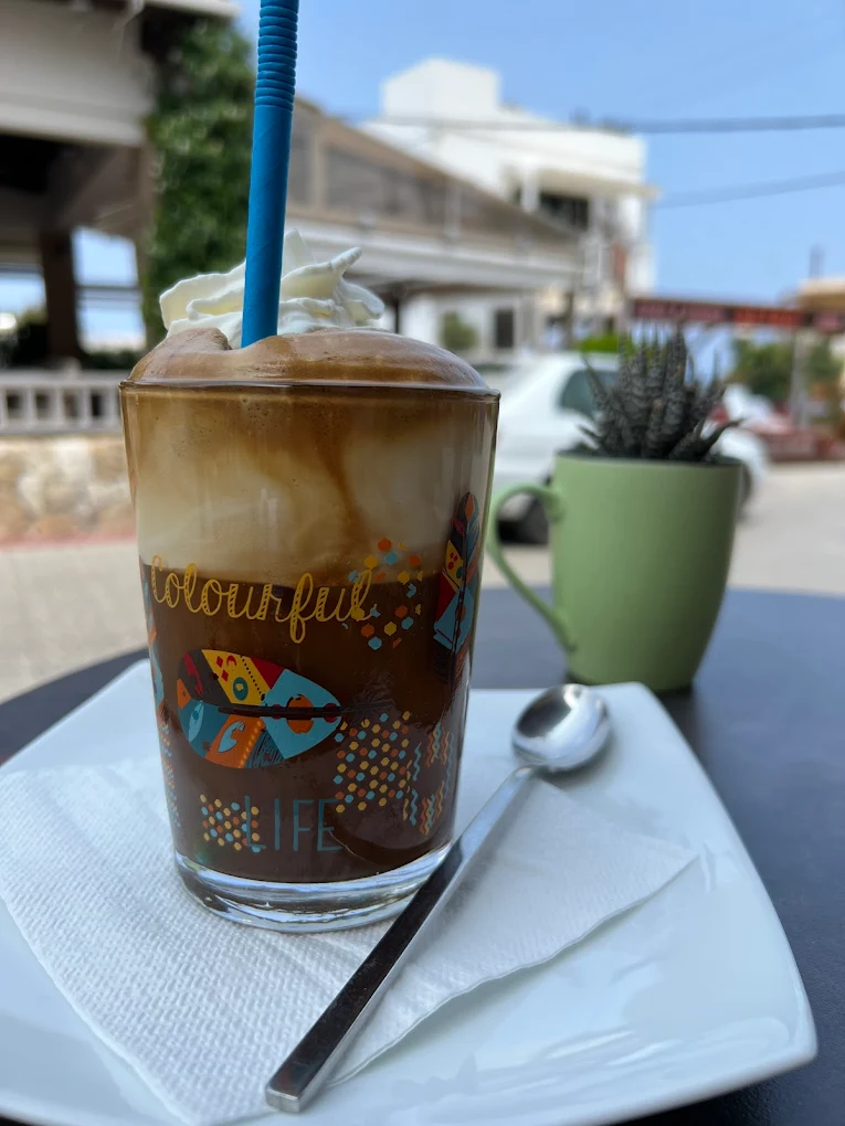 A perfectly layered iced cappuccino enjoyed on Rahati Café Patisserie Bistro's terrace in Koutouloufari village, where the relaxed yet elegant atmosphere and stunning Cretan coast views create the perfect setting for savoring quality coffee and house-made sweets.