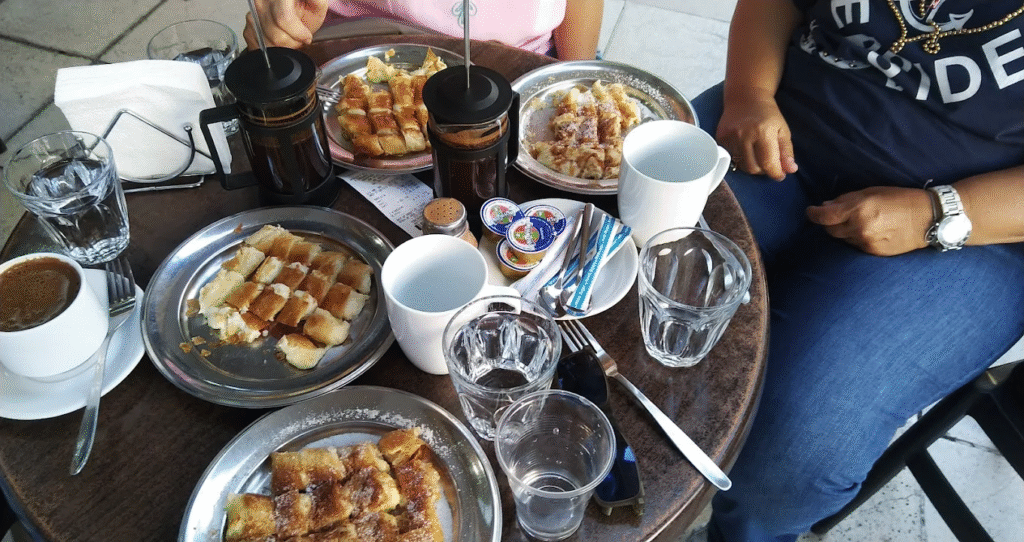 A traditional Chania breakfast spread at Bougatsa Chania featuring multiple plates of freshly made bougatsa cut into squares, served with Greek coffee and herbal tea at this beloved local favorite. 
