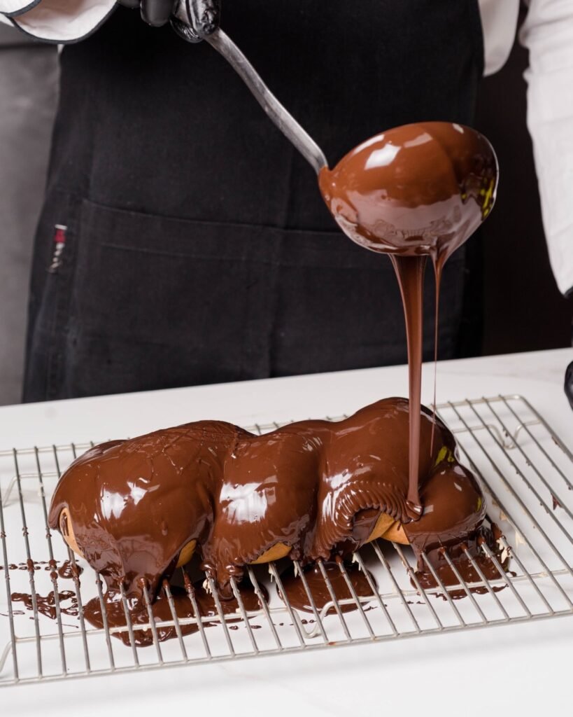 Behind the scenes at Klimatsakis, a beloved zaharoplasteio (pastry shop) in Chania, where skilled pastry chefs pour rich chocolate glaze over freshly baked desserts using classic techniques that have made this neighborhood favorite a trusted name for generations. Photo Credit: Klimatsakis