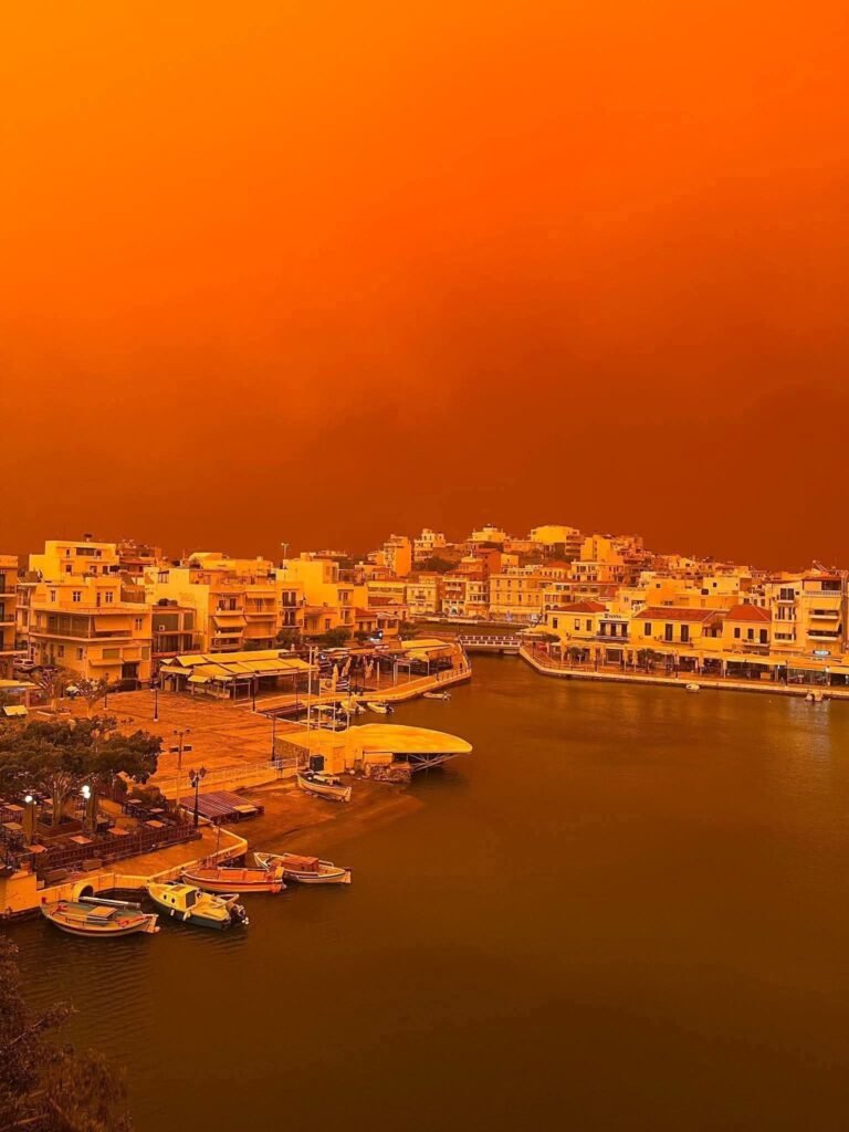 Agios Nikolaos under an intense Saharan dust sky, with the lake and waterfront glowing orange‑red on 1 April 2026. Photo: Κώστας Σινόπουλος.