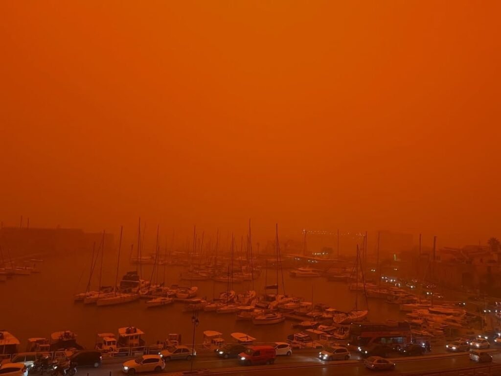 Heraklion’s old harbour under Saharan dust, with cars driving through an orange haze as visibility drops on 1 April 2026. Photo: @barstoolrode0